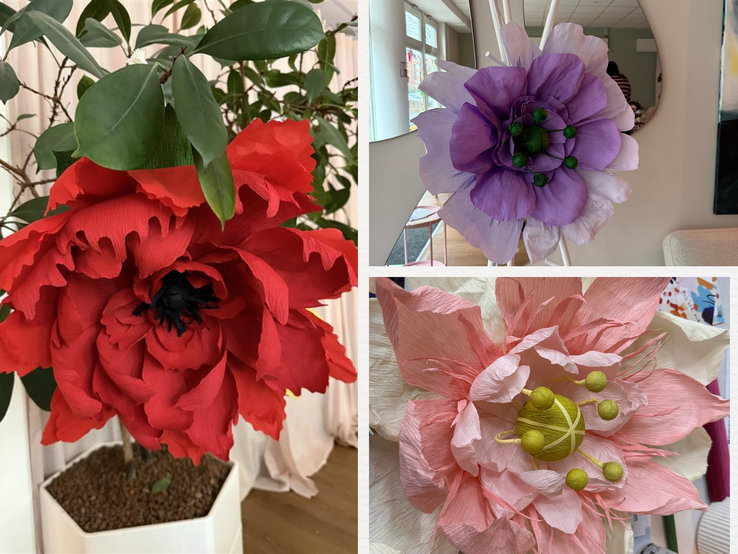 Große rote, lila und zartrosa XXL-Papierblumen mit detailreichen Blütenblättern stehen und liegen dekorativ in hellem Innenraum.