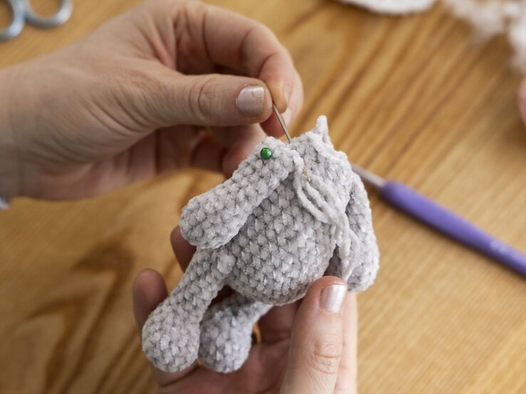 Hände halten einen halbfertigen gehäkelten grauen Stoffhasen, mit einer Nadel wird Garn eingearbeitet. | © BILD der FRAU/Photoproduction Bernd Hanselmann