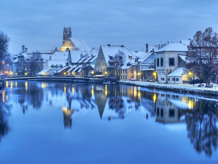 Eine verschneite Altstadt am Abend. Die Lichter spiegeln sich im Fluss.
