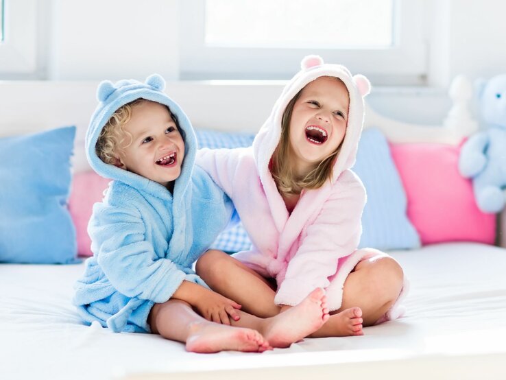 Zwei Kinder tragen Bademäntel in rosa und blau.