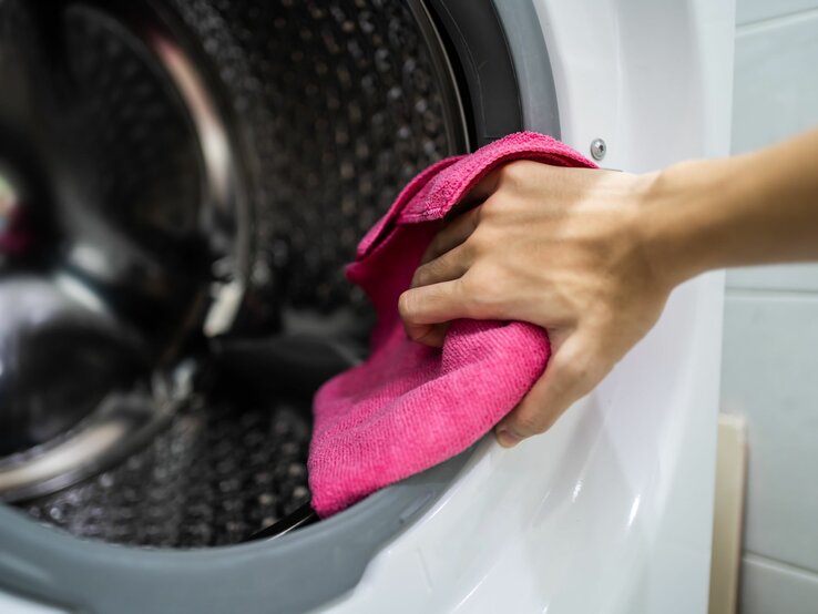 Die Hand einer Frau mit einem Lappen in der Hand, sie putzt die Trommel einer Waschmaschine 