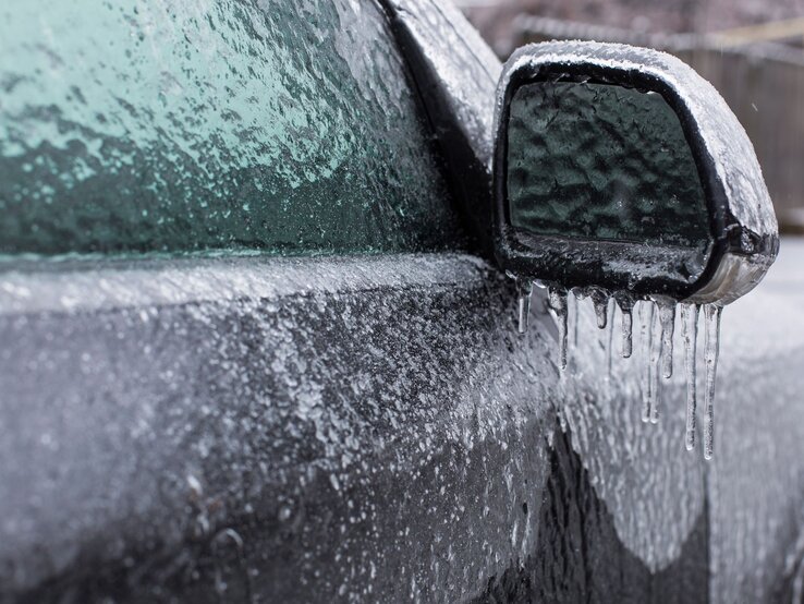 Auto Kälte Gegenstände Außenspiegel und Fenster eines Autos komplett von einer dicken Eisschicht bedeckt, an der Eiszapfen hängen.