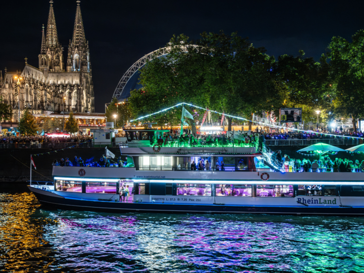 Zu sehen sind ein wunderschön beleuchtetes Boot mit dem Kölner Dom im Hintergrund