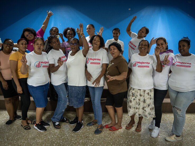 Fünfzehn fröhliche Frauen verschiedener Alters posieren lachend und gestikulierend vor blauer Wand in einem Gruppenraum. | © Martin Hanebeck