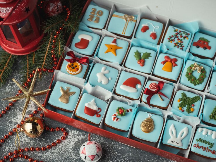 Detailreicher Adventskalender mit 24 bunt verzierten Weihnachtskeksen in Blau, Rot und Gold in festlicher Geschenkbox.