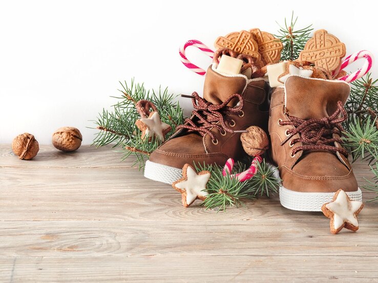 Nikolaus Sprüche: Gefüllte Winterstiefel mit Zuckerstangen, Nüssen und Zimtsternen stehen festlich zwischen Tannengrün auf Holz.