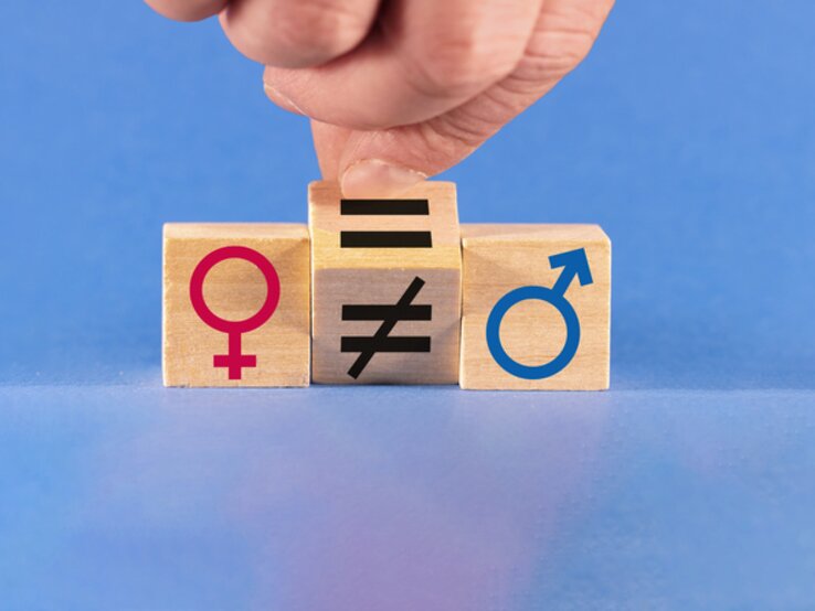 Eine Hand verändert ein Ungleichheitszeichen in ein Gleichheitszeichen zwischen männlichen und weiblichen Symbolen.