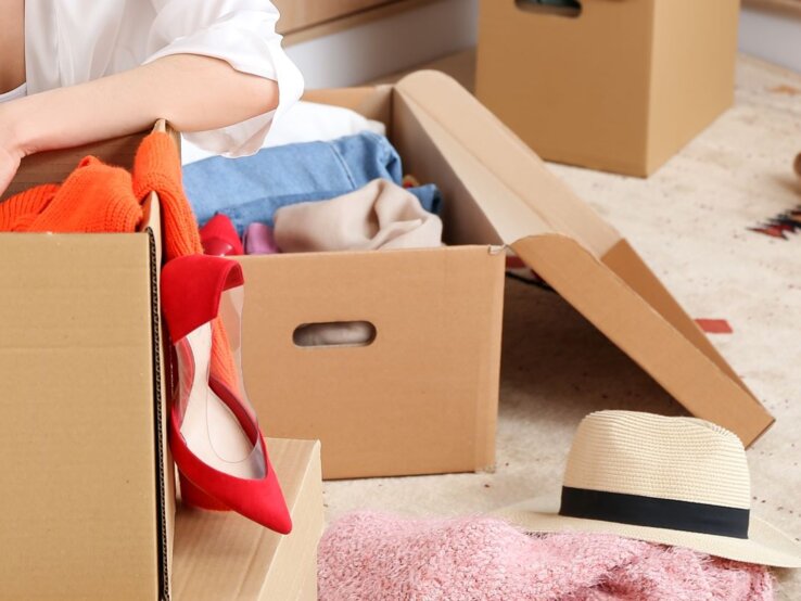 Eine junge Frau sitzt überfordert zwischen mehreren vollgestopften Kartons.