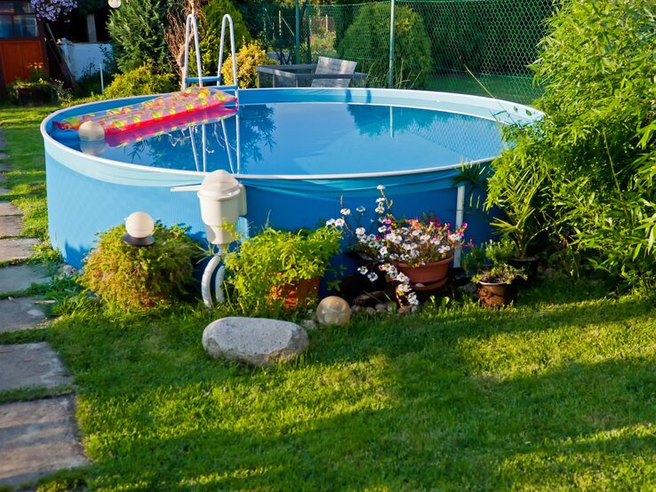 Ein gepflegter Garten mit frisch gemähtem Rasen, blühenden Pflanzen und einem runden Pool, in dem sich die Umgebung spiegelt.
