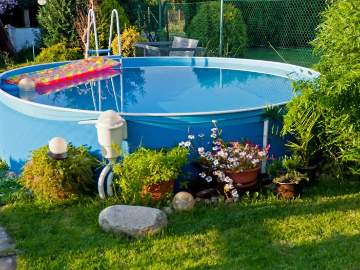 Ein gepflegter Garten mit frisch gemähtem Rasen, blühenden Pflanzen und einem runden Pool, in dem sich die Umgebung spiegelt.