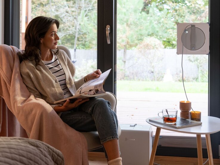 Eine Frau sitzt im Sessel und sie schaut zum Fenster, das ihr ECOVACS- Reinigungsroboter reinigt.