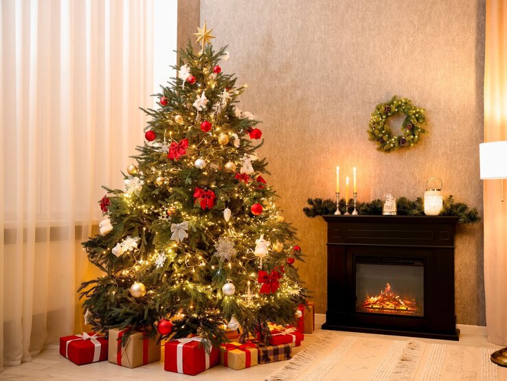 Geschmückter Weihnachtsbaum mit roten Schleifen und glänzenden Kugeln, daneben leuchtender Kamin mit Kerzen und Tannendekor.