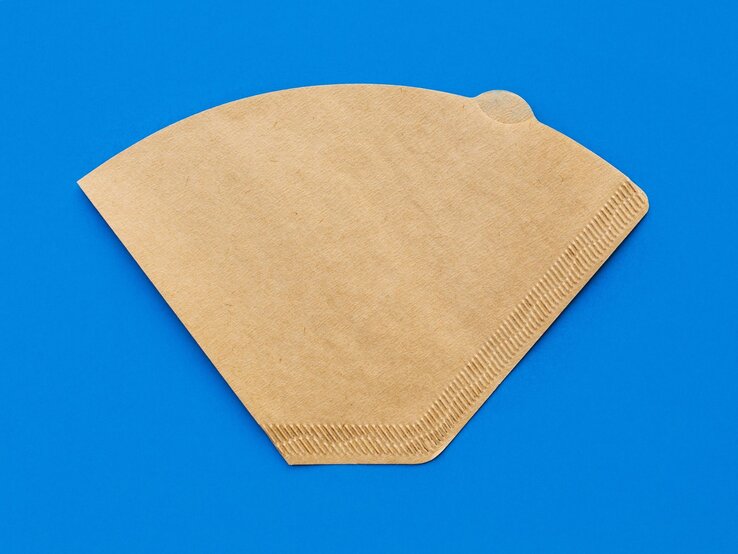 Ein brauner Kaffeefilter mit deutlich sichtbaren Rillen liegt flach auf einem kräftig blauen Hintergrund. | © Shutterstock/makanna