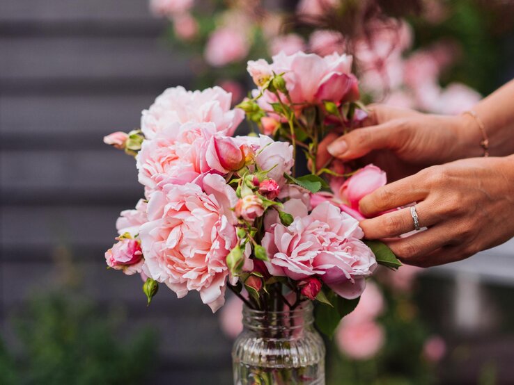 Eine Frau drapiert Rosen in einer Vase draußen. 