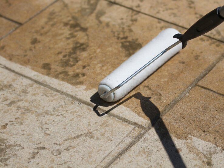 Jemand trägt eine Versiegelung auf Terrassenplatten mit einer Rolle auf. 