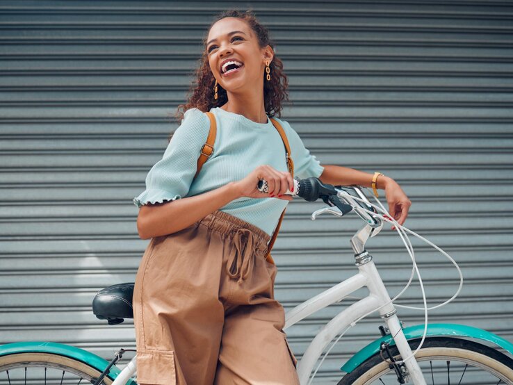 Junge, lächelnde Frau schiebt ein Fahrrad