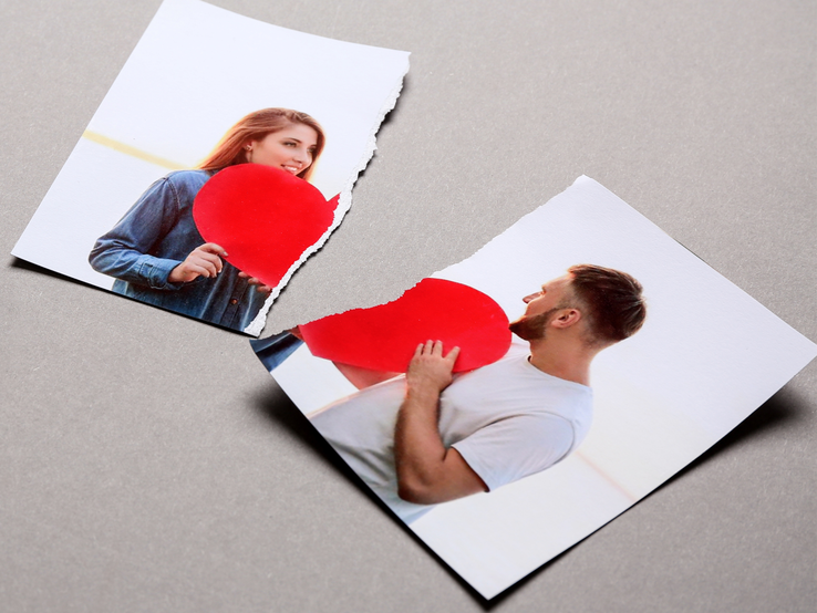 Zerrissenes Foto auf grauem Untergrund zeigt zwei Personen, jeweils mit einem roten Herz vor sich, getrennt durch einen Riss.