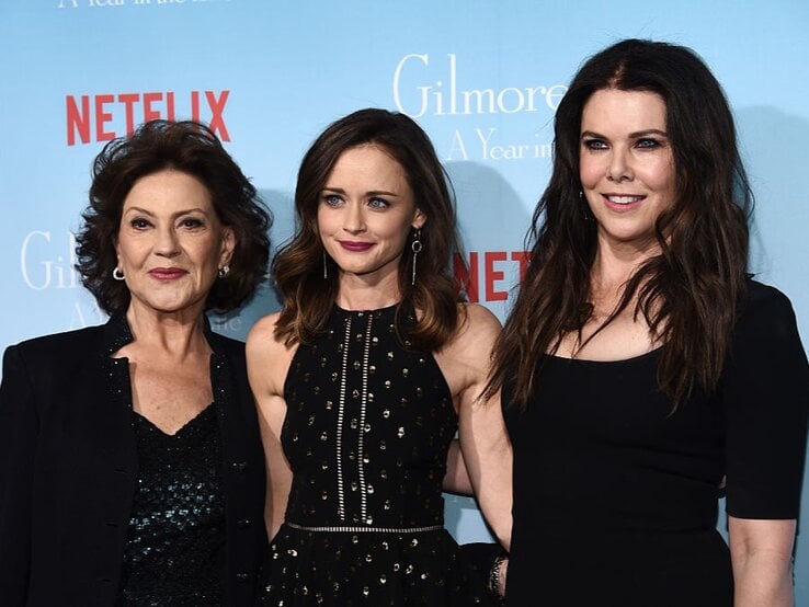 Drei Frauen stehen vor einer blauen Wand mit Netflix-Logo, stilvoll gekleidet in Schwarz, lächelnd und eng nebeneinander.