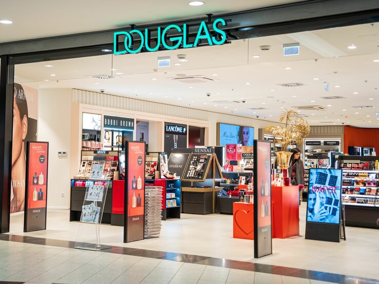 Haupteingang des Douglas-Kosmetikgeschäfts mit beleuchtetem Logo und verschiedenen Beauty-Marken.