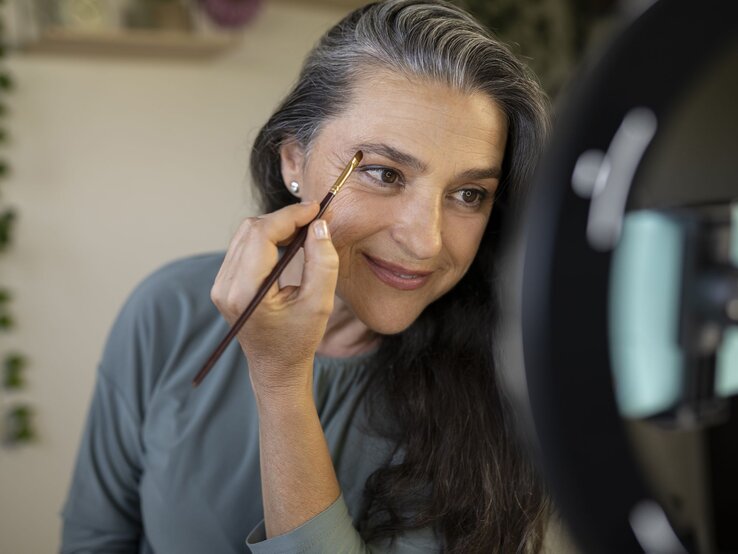 Make up tutorial Frauen ab 50 Zu sehen ist eine lächelnde Frau mittleren Alters, die sich schminkt