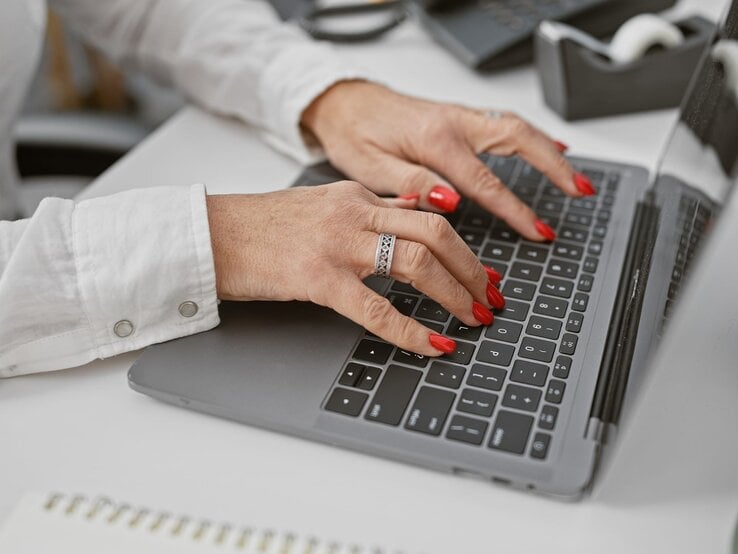 Rote Fingernägel Theorie Psychologie Gepflegte Frauenhände mit rotem Nagellack und silbernem Ring tippen auf einer Laptop-Tastatur in modernem Büroambiente.