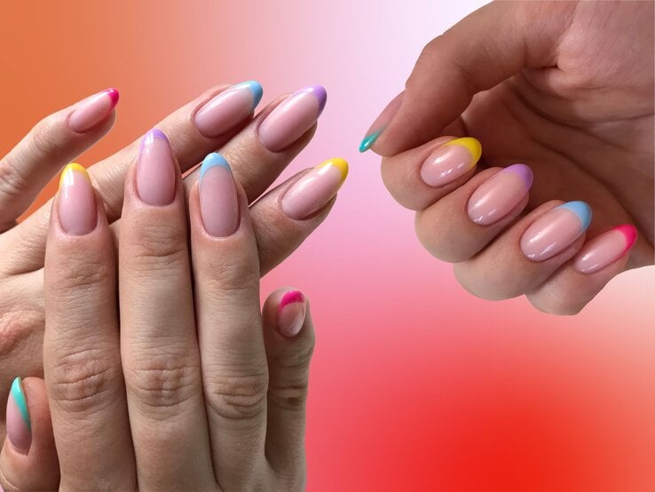 Colored French Nails Nahaufnahme zweier Hände mit glänzender Maniküre in pastellfarbenen French-Nail-Spitzen vor rot-pinkem Hintergrund.