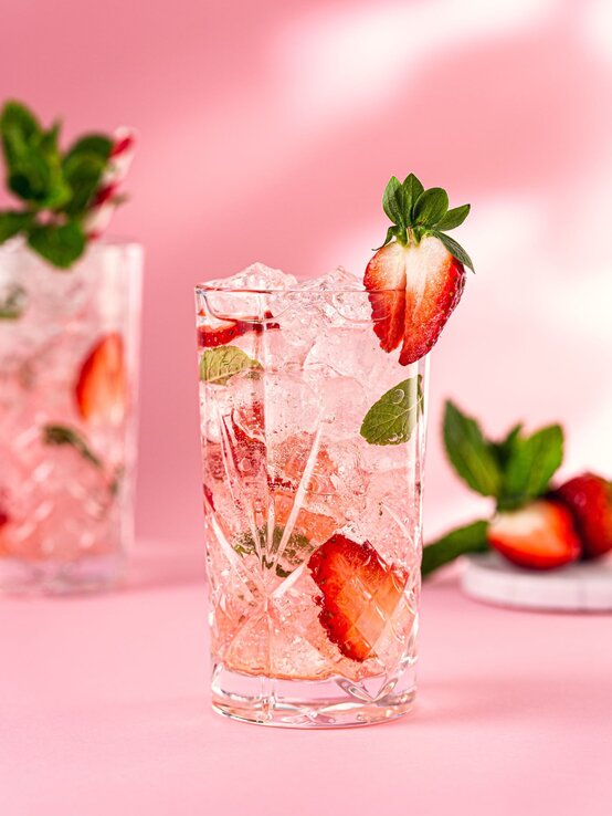 Kollagen Wasser Drink | © Iryna Melnyk/ Glow25 Kristallglas mit Erdbeer-Minz-Drink und Crushed Ice vor pinkem Hintergrund, garniert mit halber Erdbeere am Glasrand. | © Iryna Melnyk/ Glow25