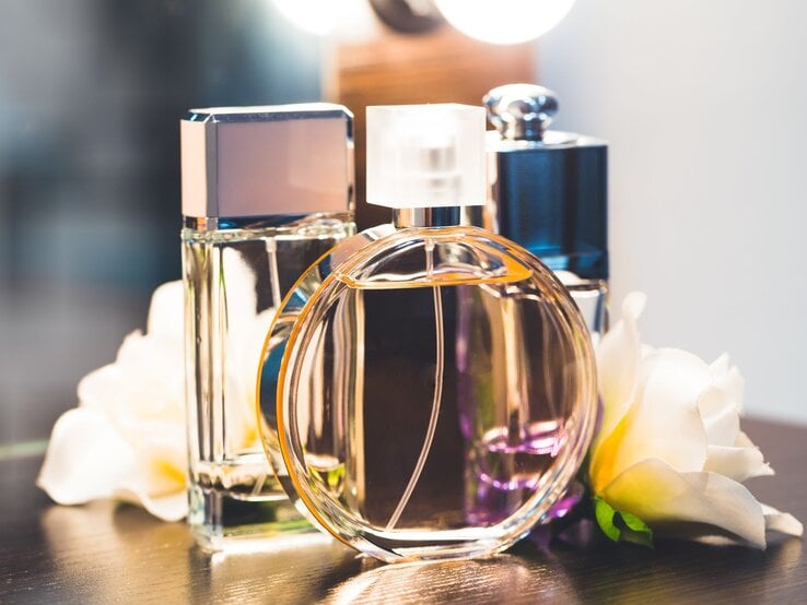 Parfum falsch lagern Badezimmer Drei elegante Parfümflakons in verschiedenen Formen stehen auf einem dunklen Tisch, umgeben von weißen Blumen und warmem Licht.