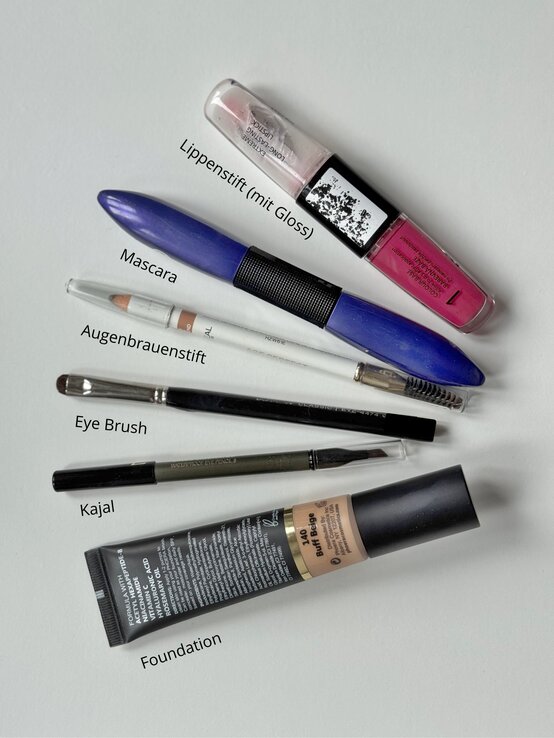 Renate Zott 6 Minuten Make-up Tools | © Renate Zott Verschiedene Make-up-Produkte, darunter Lippenstift, Mascara, Augenbrauenstift, Kajal, Pinsel und Foundation, liegen auf einer weißen Fläche | © Renate Zott