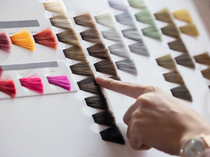 Welche Haarfarbe passt zu mir? Finger deutet auf verschiedene Haarfarbemuster, von Blond bis Schwarz.