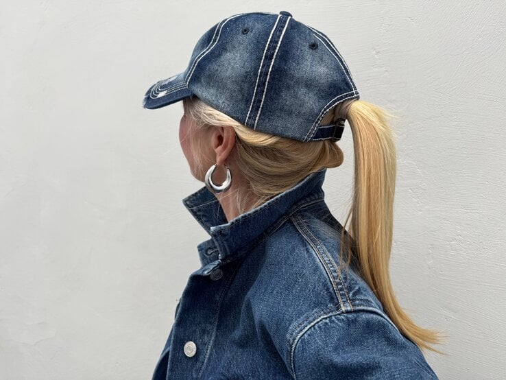 Renate Zott Bad Hair Day Sommer Cap plus Pferdeschwanz | © Renate Zott Blondhaarige Renate Zott mit Pferdeschwanz und silbernen Creolen trägt Jeansjacke und Baseballcap, im Profil vor grauer Wand. | © Renate Zott