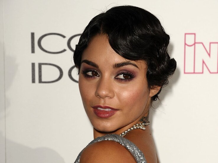 Vanessa Hudgens | © Getty Images / Jason LaVeris Junge Frau mit dunklem, gewelltem Bob und silbernem Kleid blickt mit sinnlichem Ausdruck über die Schulter in die Kamera. | © Getty Images / Jason LaVeris