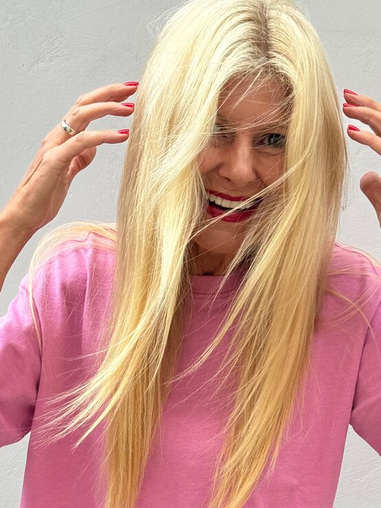 Lachende Renate Zott in pinkem Shirt streicht sich mit roten Fingernägeln die Haare aus dem Gesicht. | © Renate Zott