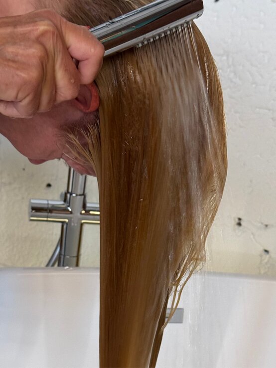 Nasses, blondes Haar wird unter fließendem Wasserstrahl über der Badewanne mit der Hand und einer Bürste ausgespült. | © Renate Zott