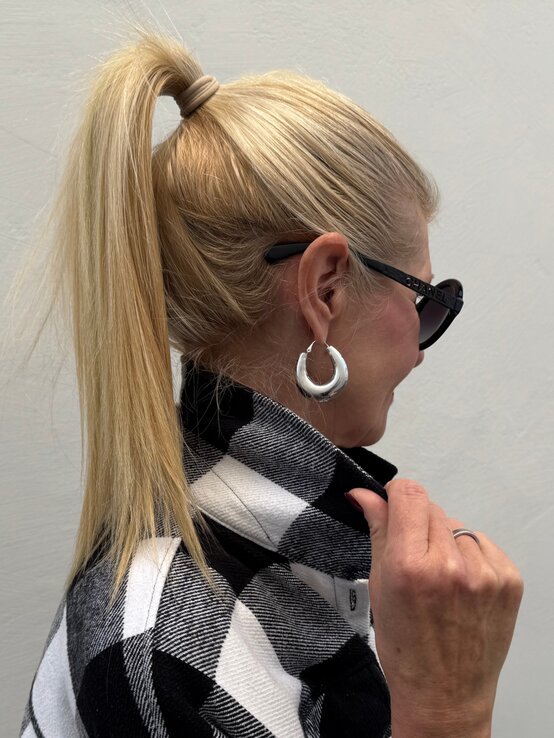 Profilansicht einer Frau mit hochgebundenem blondem Haar und kariertem Mantel, ergänzt durch große silberne Ohrringe. | © Renate Zott