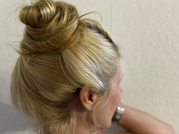 Blond hochgestecktes Haar in einem kunstvollen Dutt mit lockeren Strähnen, schlicht präsentiert vor einer beigefarbenen Wand. | © Renate Zott 