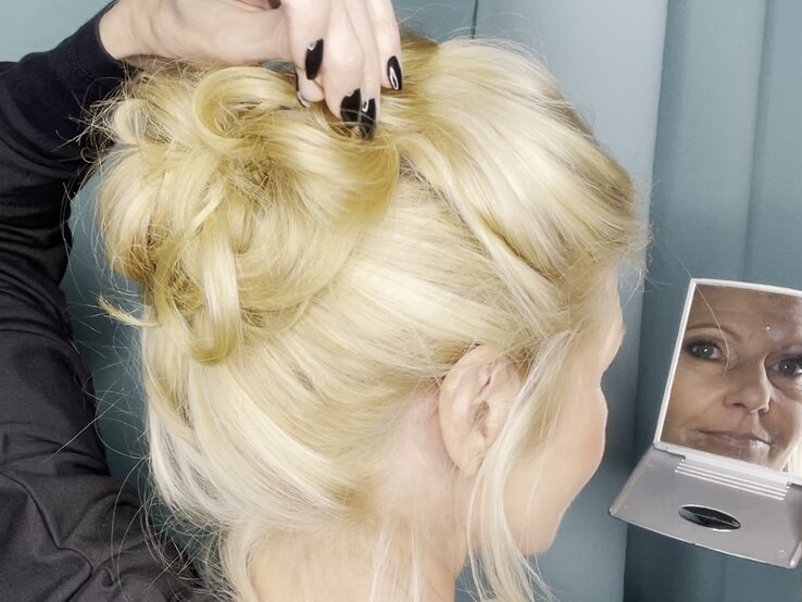 Hochgesteckte blonde Frisur in elegantem Look, formvollendet gestylt, mit einer Hand, die Details betont, vor einem türkisfarbenen Hintergrund. | © Renate Zott 