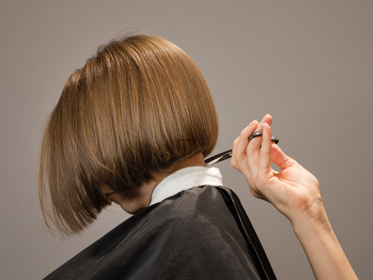 Ein Bob-Haarschnitt mit glänzendem, glattem, braunem Haar wird präzise von einer Hand mit Schere geschnitten.