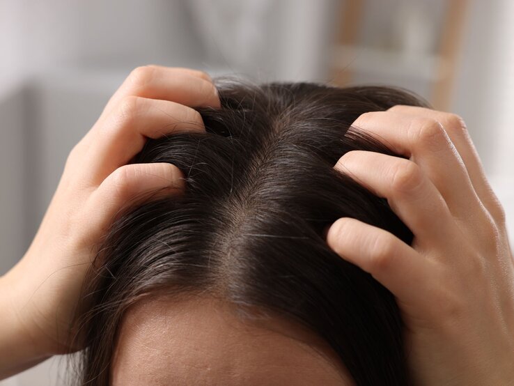 Eine Person mit dunklem Haar drückt ihre Fingerspitzen gegen die Kopfhaut, offenbar bei einer wohltuenden Kopfmassage.