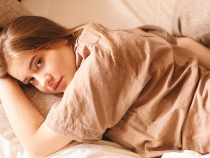 Junge Frau trägt einen Leinenhemd und liegt auf einer Leinen-Bettwäsche. | © Getty Images/Cavan Images