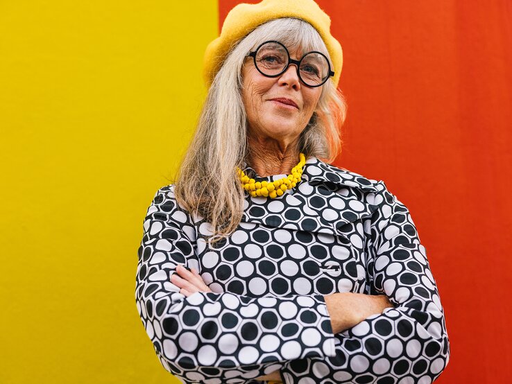Frau um 65 Jahre trägt ein Oberteil mit auffälligem Muster und kombiniert dazu einen gelben Hut und Kette. | © Getty Images/jacoblund
