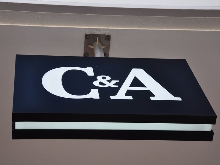 Das Foto zeigt das Logo einer C&A Filiale auf einem Schild. Die Schrift ist weiß, das Schild Schwarz gehalten.