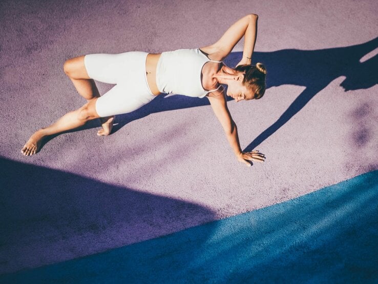 Eine Frau im weißen Sportdress macht Yogaübungen auf dem Boden.