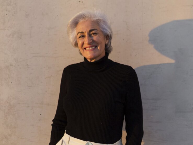 Rollkragen Bonprix Elegante Frau mit grauem Haar in schwarzem Rollkragenpullover und heller Hose lehnt lächelnd vor einer Betonwand mit weichem Schatten.