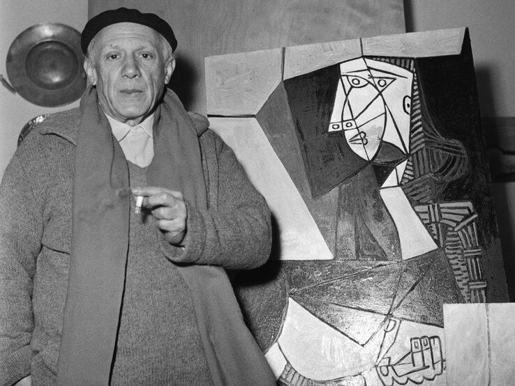 Künstler Pablo Picasso in schlichter Kleidung und Baskenmütze präsentiert sein kubistisches Gemälde.