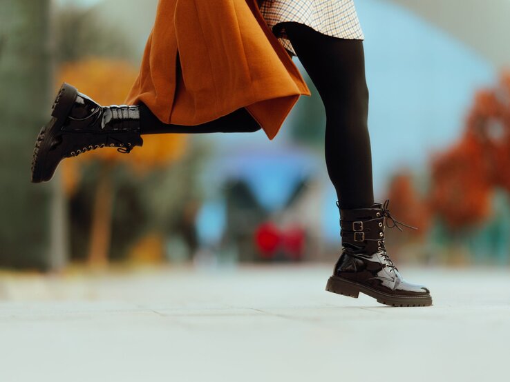 Stiefel Winter Lidl Schwarze, glänzende Stiefel mit dicker Sohle und Schnallen in Bewegung, getragen mit kariertem Rock und braunem Mantel.