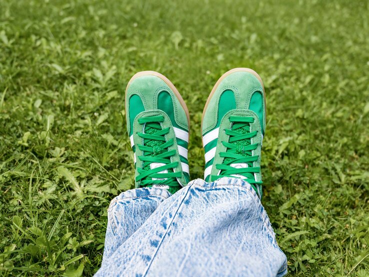 Füße in kräftig grünen Adidas Samba Sneakern ruhen locker auf sommerlicher Wiese, die Jeans ist locker über die Schuhe gelegt.