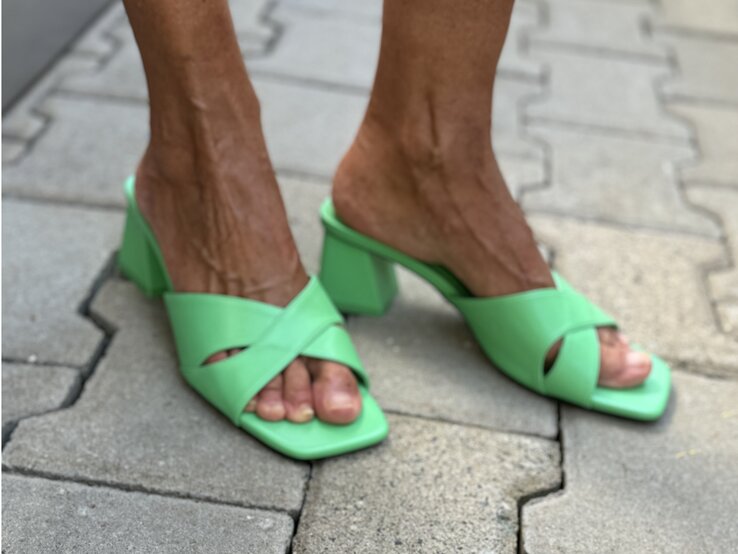 Leuchtend grüne Mules mit breiten Kreuzriemen und Blockabsatz an gebräunten Füßen auf hellen Pflastersteinen. | © Renate Zott