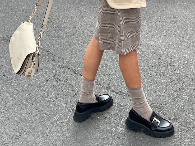 Beine in kariertem Rock, beige Söckchen und schwarzen Chunky-Loafern mit goldener Schnalle auf grauem Asphalt. | © Renate Zott