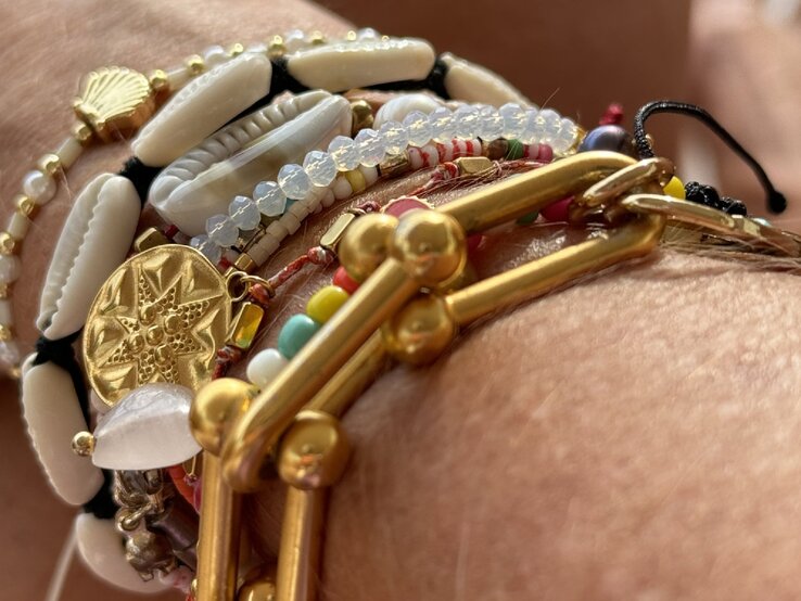 Anti-Aging-Accessoires: Nahaufnahme mehrerer bunter Armbänder mit Muscheln, Goldanhängern und Perlen an Renate Zotts gebräunten Handgelenk. | © Renate Zott